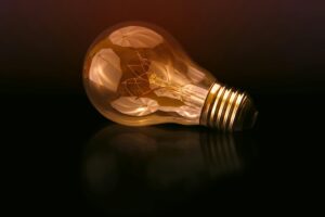 A glowing incandescent lightbulb resting on a dark reflective surface, symbolizing a new idea or innovation.