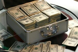 A metal briefcase overflowing with stacks of hundred-dollar bills, symbolizing financial success and high profitability.