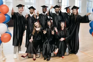 A diverse group of smiling graduates wearing caps and gowns pose together indoors, symbolizing the success and challenges of students navigating higher education.