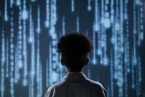 A young student viewed from behind, standing in front of a large screen displaying cascading lines of digital code, symbolizing the integration of AI and technology in modern education.
