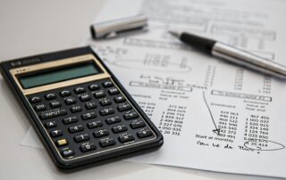 A calculator and financial documents with handwritten notes and figures, representing the detailed review and preparation needed for HR or financial audits.