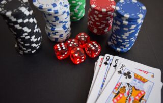 Stacks of casino poker chips, red transparent dice, and a hand of playing cards featuring a King of Clubs on a dark surface, serving as a conceptual metaphor for financial risk management and strategic business decisions.